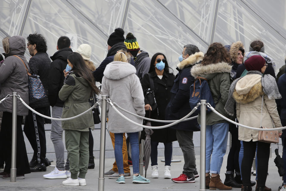 Tourists, some wearing a mask, queue to enter the Louvre museum Friday, Feb. 28, 2020 in Paris. . The world is scrambling to get on top of the new coronavirus outbreak that has spread from its epicenter in China to most corners of the planet. Governments and doctors are presenting an array of approaches as the virus disrupts daily routines, business plans and international travel around the world (AP Photo/Rafael Yaghobzadeh)