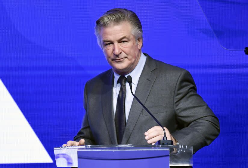 An man in a gray suit stands behind a lectern and in front of a bright blue backdrop