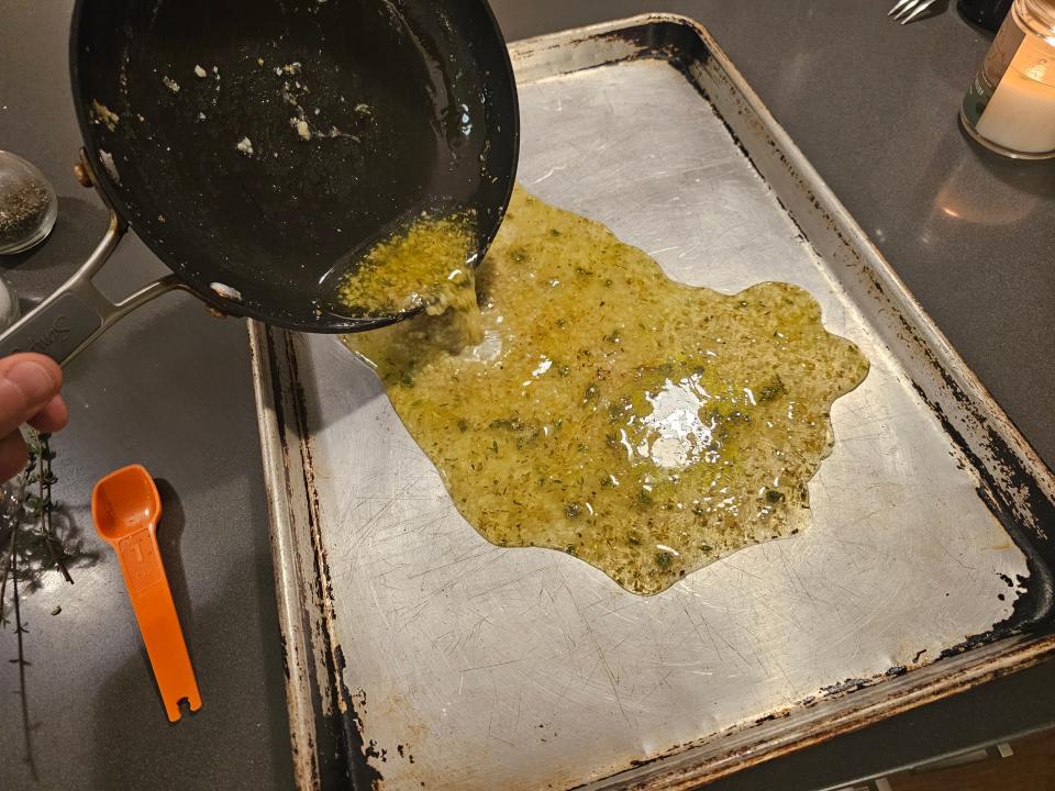 Pouring pan of hot, seasoned oil onto a metal baking sheet