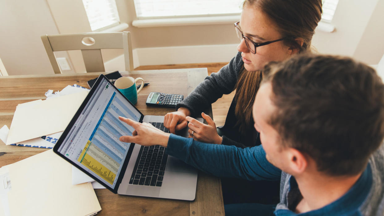 A young millennial married couple are doing their monthly budget at a kitchen dining room table in their home.