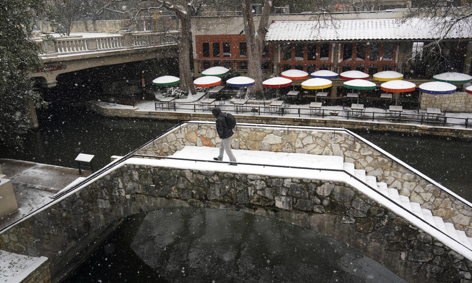 A man crosses a bridge along the River Walk as snow falls, Thursday, Feb. 18, 2021, in San Antonio. Snow, ice and sub-freezing weather continue to wreak havoc on the state's power grid and utilities. (AP Photo/Eric Gay)