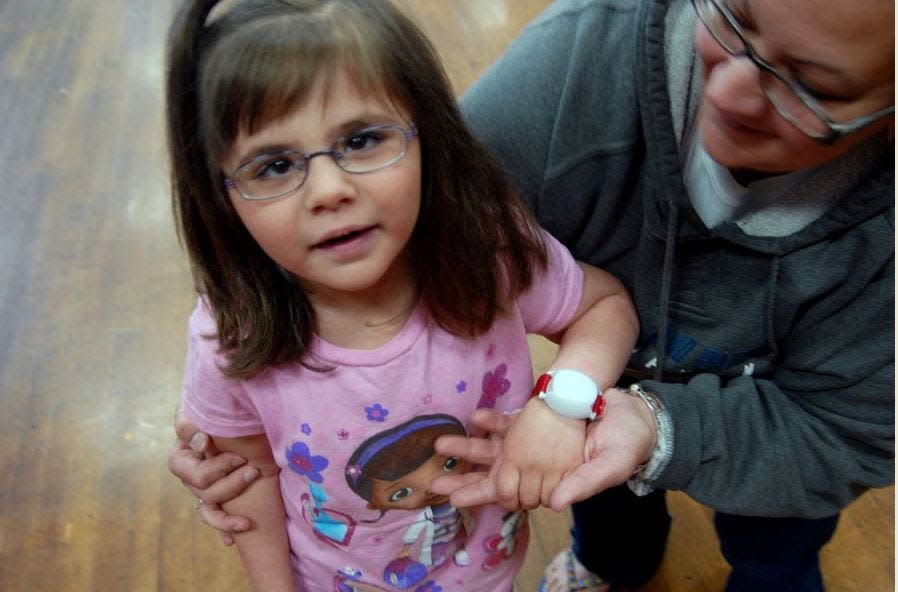 Five-year-old Emily Santarpia, seen here with her mother Maria in 2014, shows off her Project Lifesaver bracelet that allows law enforcement to track people with autism and Alzheimer's who have wandered off. Emily's parents organized a walk to benefit Project Lifesaver. Emily died on Jan. 30, 2023 from complications of a rare genetic condition, isodicentric 15.
