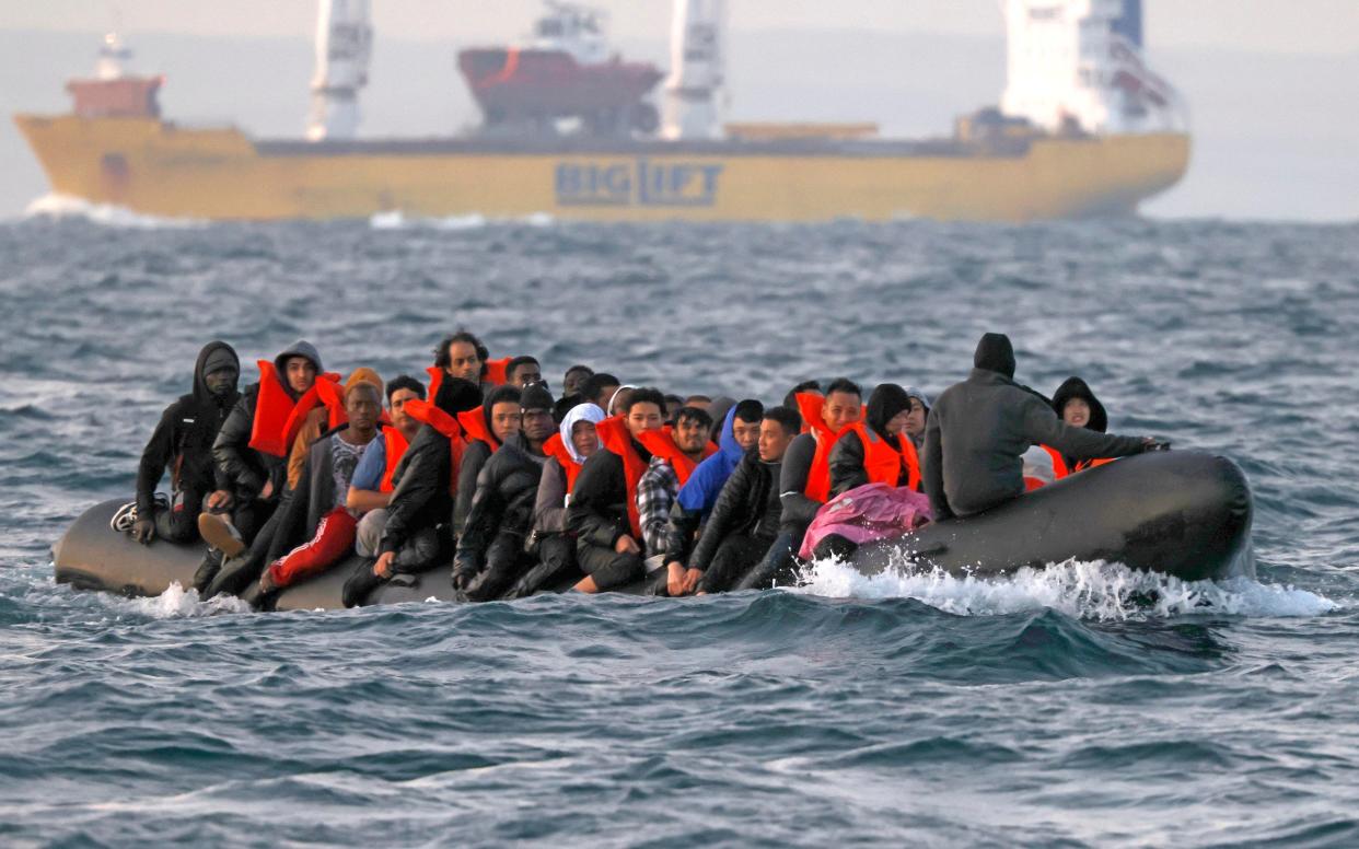 An inflatable rubber boat carries a large number of young men, some wearing life vests