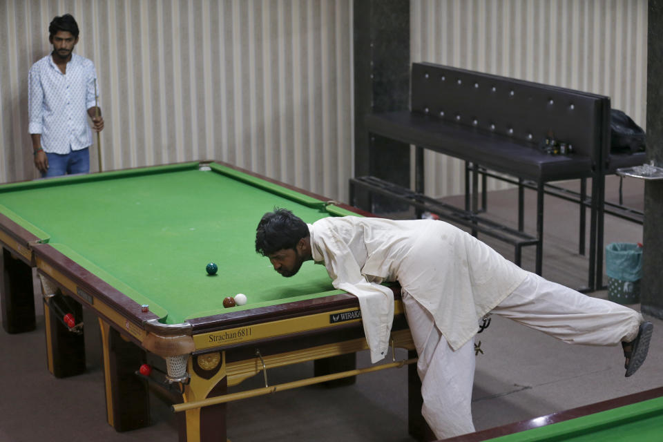 Mohammad Ikram plays snooker with his chin at a local snooker club in Samundri town, Pakistan, Sunday, Oct. 25, 2020. Ikram, 32, was born without arms, but everyone simply admires his snooker skills when he hits the cue ball with his chin and pots a colored ball on a snooker table. He lives in a remote rural town of Punjab province and his physical disability doesn't come in his way to fulfil his childhood dream of playing the game of snooker. (AP Photo/Anjum Naveed)