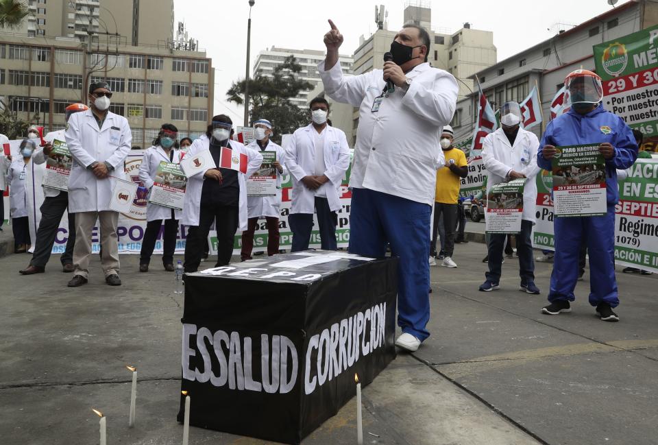 Trabajadores de la salud se paran alrededor de un ataúd simulado con la palabra "corrupción" y al nombre de la aseguradora nacional de salud de la entidad de seguridad social (ESSALUD) mientras protestan por la falta de equipo de protección para el personal que atiende a pacientes con COVID-19, frente a un hospital público en Lima, Perú, el martes 29 de septiembre de 2020. (AP Foto/Martín Mejía)