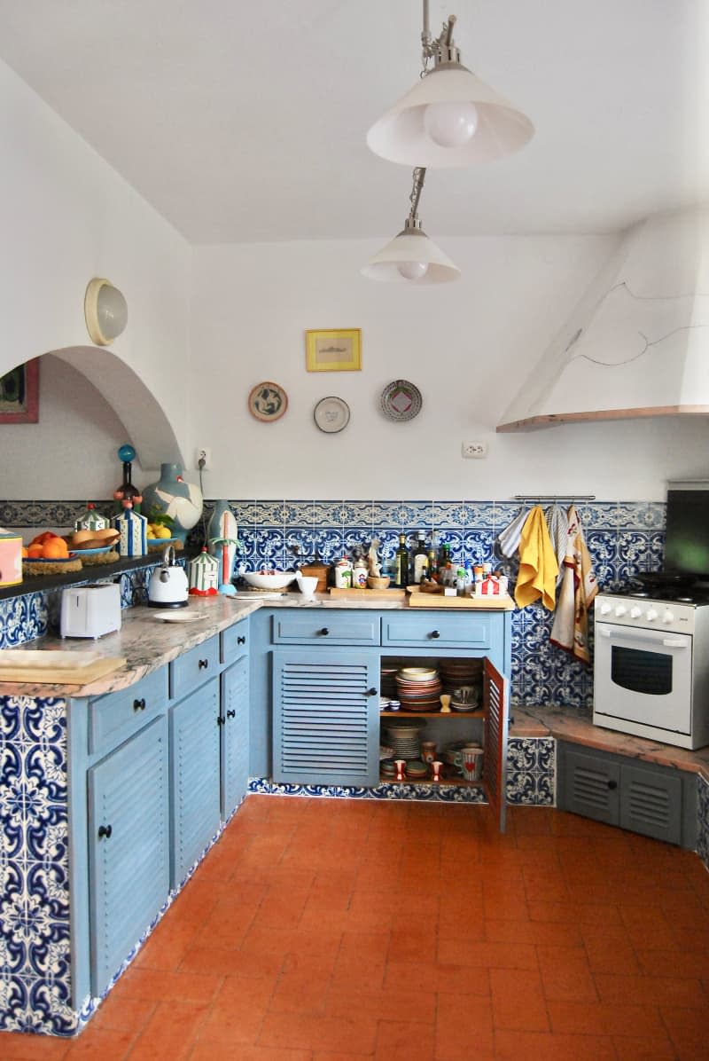 Kitchen with blue tile and cabinets, and white stove raised in corner.