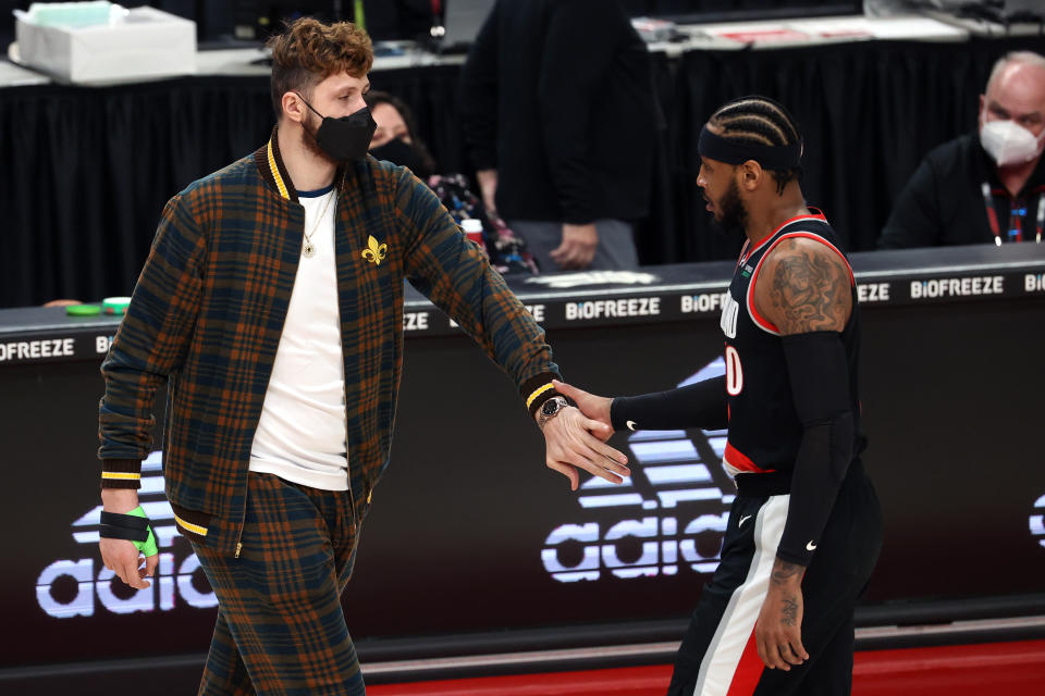 Jusuf Nurkic, in normal clothes, slaps hands with Carmelo Anthony who is walking off the court during a game.