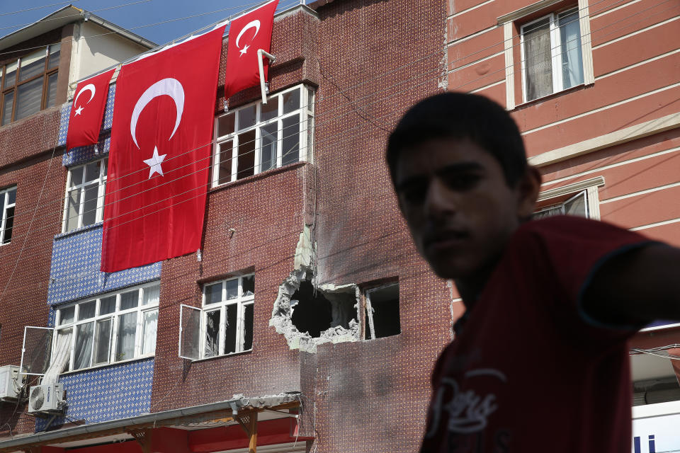 FILE-In this Sunday, Oct. 13, 2019 file photo, a child stands across from a building damaged by a mortar fired from inside Syria, in the border town of Akcakale, Sanliurfa province, southeastern Turkey. Since Turkey announced its incursion into neighbouring Syria to clear out Kurdish fighters last week, patriotic sentiment has run high, with national emblems being proudly displayed. (AP Photo/Lefteris Pitarakis, File)