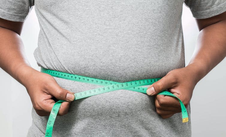 Overweight man using a measuring tape to measure his midsection.