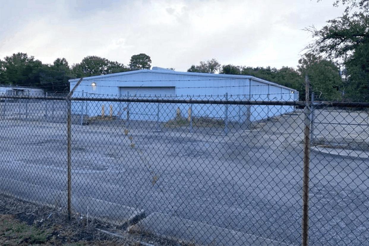 A blue warehouse behind a chain-link fence.