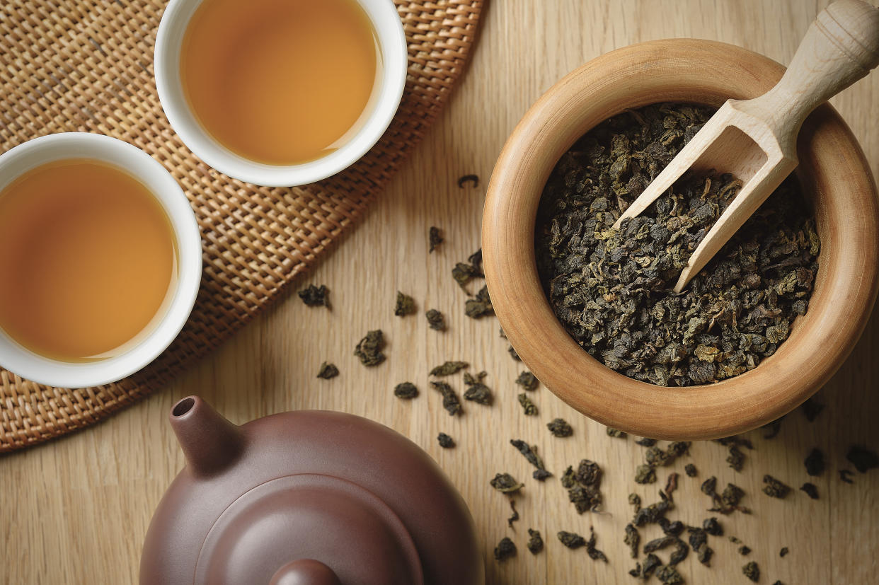 Tea leaves spilling out from wooden bowl, near the Freshly brewed tea