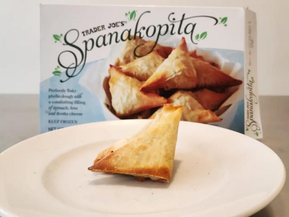 A white plate with a light brown spanakopita pastry. A blue box sits behind plate