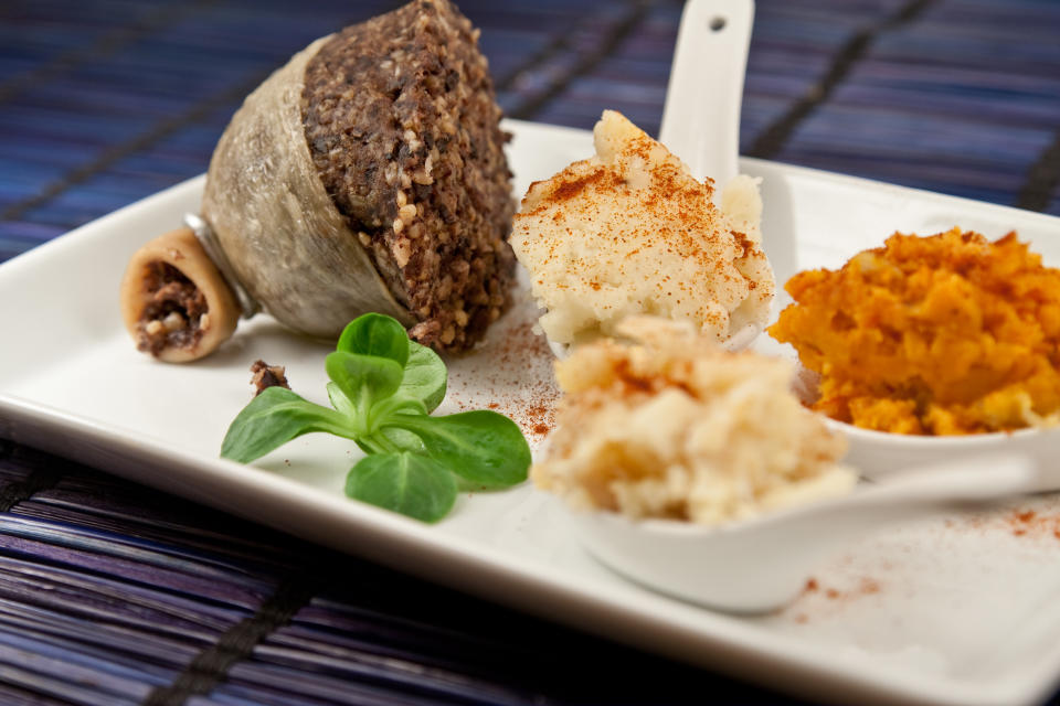 Haggis and turnip and potato mash and sweet potato mash presented in a plate with a cooked half haggis and a lamb&#39;s leaf lettuce, traditional food of Scotland presented in a modern way