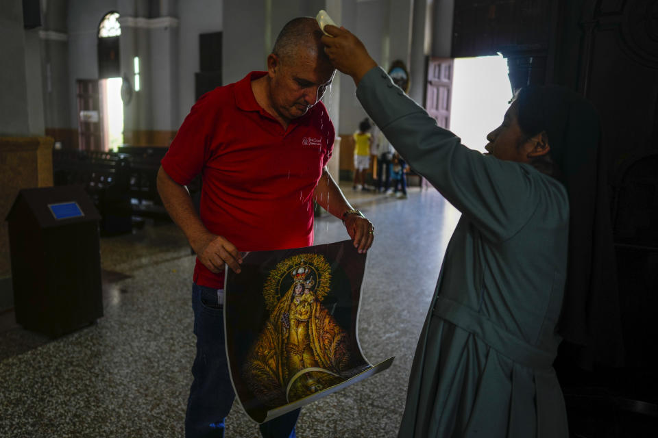 Ramón Nieblas es bendecido por una monja mientras sostiene un afiche de la Virgen de la Caridad del Cobre en el santuario de la santa patrona de Cuba en El Cobre, Cuba, el domingo 11 de febrero de 2024. (AP Foto/Ramón Espinosa)