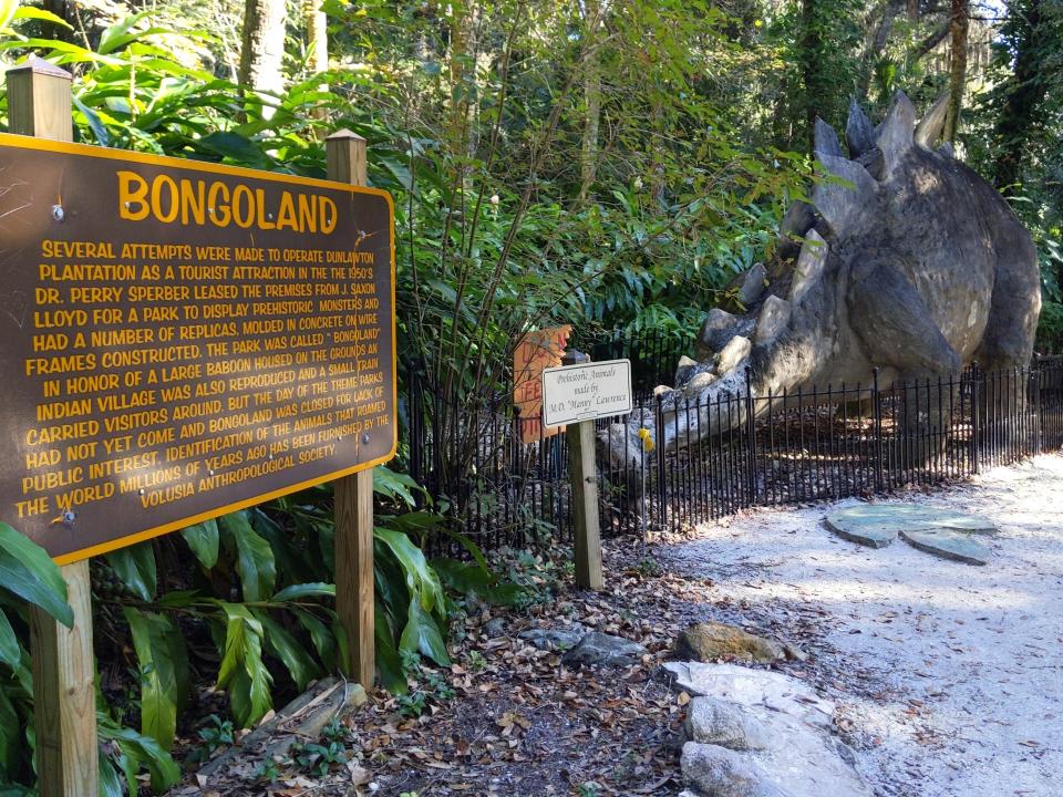 A sign for Bongoland explaining the history of the park and a statue of a dinosaur.