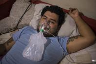 Breathing oxygen from a cylinder that was brought to him by his stepfather, Mario Solis who is suffering from COVID-19, lies isolated in an upstairs room at his home in Lima, Peru, Thursday, June 11, 2020. (AP Photo/Rodrigo Abd)