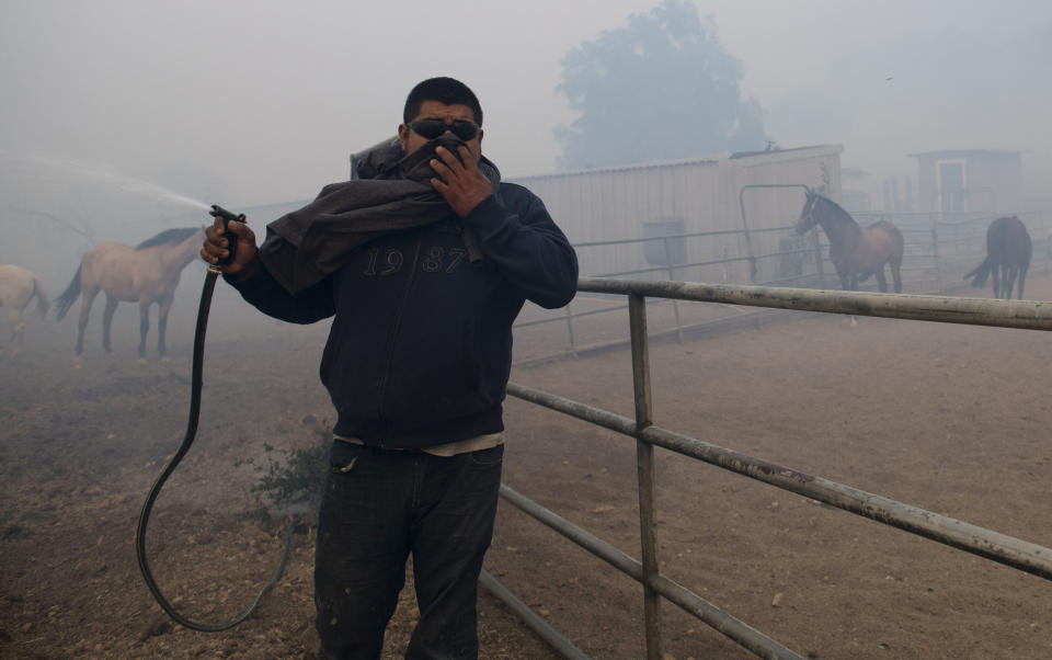 Alejandro Garrido sprays a water hose at a horse ranch as smoke from wildfires burning in the region fills the air in Simi Valley, Calif., Oct. 30, 2019. A brush fire broke out just before dawn in the Simi Valley area north of Los Angeles. (Photo: Christian Monterrosa/AP)