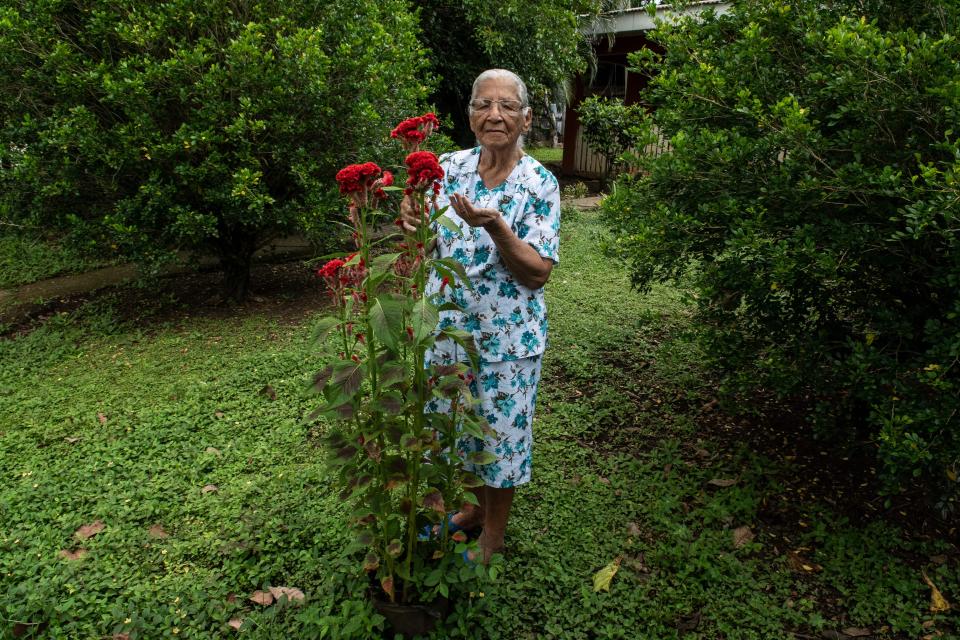 Clementina Espinoza, 91, takes care of her garden in Nicoya, Costa Rica, August 27, 2021. She attends to a red flower, and is wearing a matching two-piece blue floral set. 