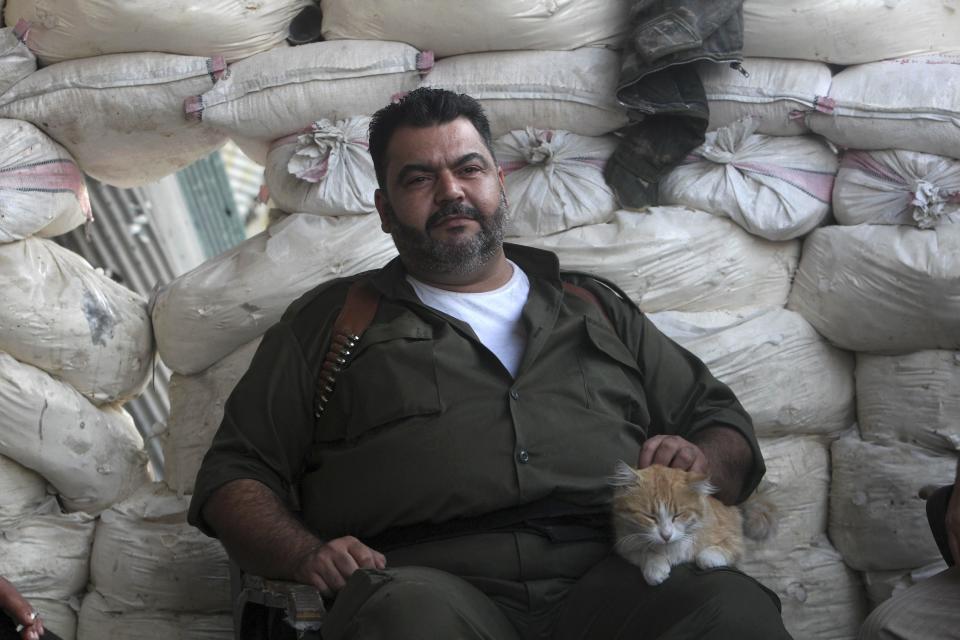 A Free Syrian Army fighter strokes a cat while sitting behind sandbags in Aleppo