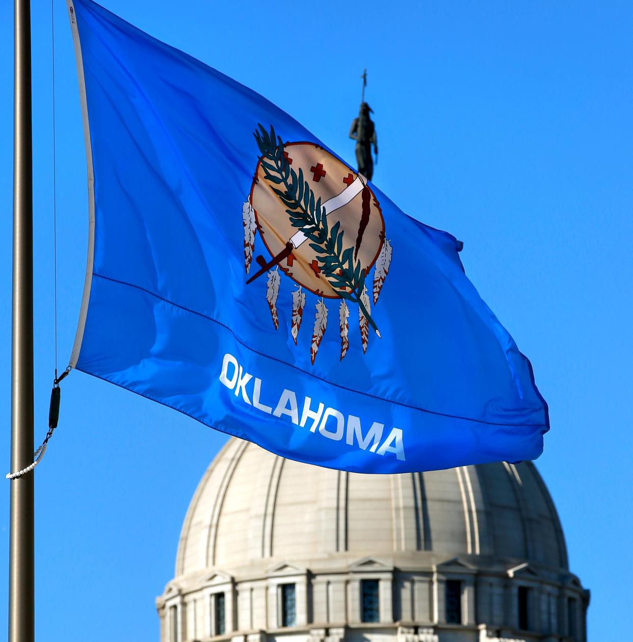 According to the Oklahoma Historical Society, the Oklahoma flag features an Osage warrior’s shield on a blue background. An olive branch and a calumet, or peace pipe, lay across the shield. Seven eagle feathers decorate the shield. Behind it, "The Guardian" can be seen atop the Capitol dome. The statue was designed by the late state Sen. Enoch Kelly Haney. The Historical Society describes it as a combination of spiritual, material and cultural characteristics of the 39 tribes in Oklahoma. Oklahoma is the first state to have a Capitol building featuring an Native American sculpture on its dome.
