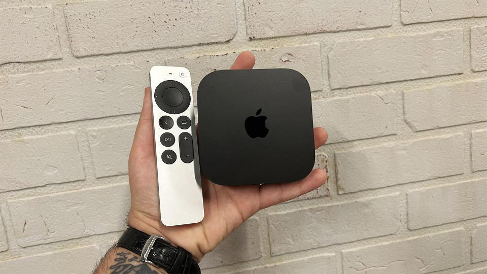 Apple TV 4K with its remote control held in front of a brick wall