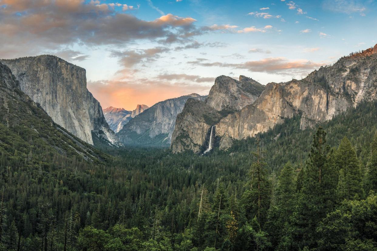 Sunset paroromic view of Yosemite National Park, California, forest in foreground with mountains and a waterfall in the background
