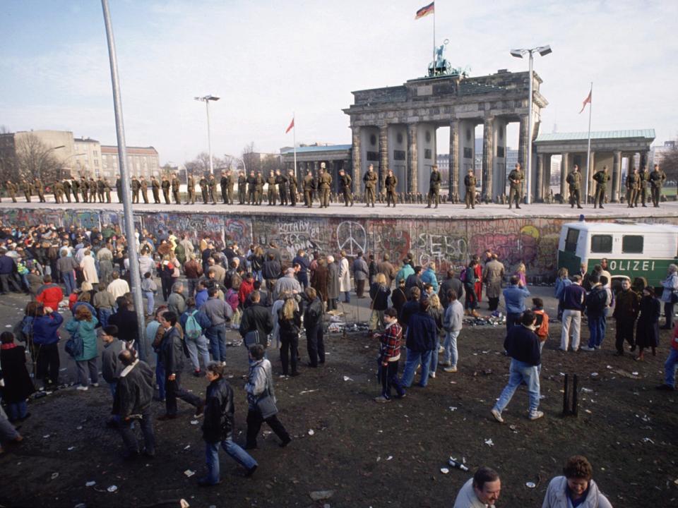 People gather on one side of the Berlin Wall, as German soldiers stand on a raised platform before the Brandenburg gate