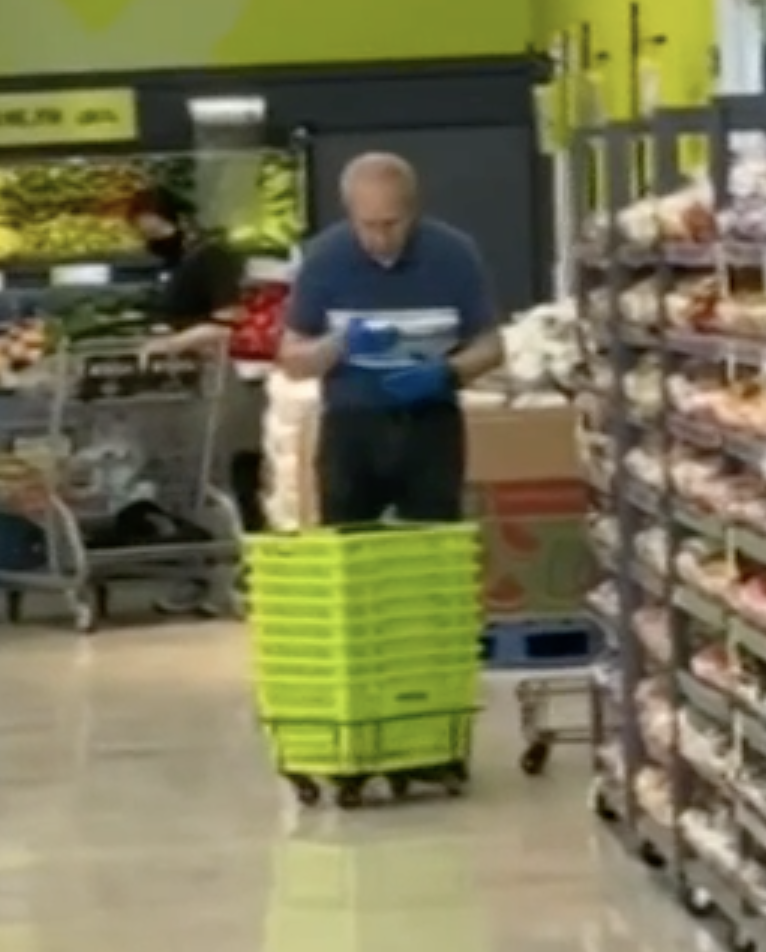 Photo shows a man spitting into a cloth before using it to clean supermarket baskets.