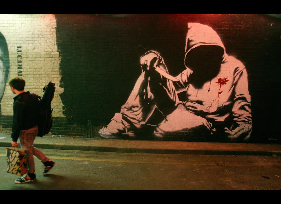 A man walks past a Banksy graffiti artwork during 'Cans' graffiti exhibition in London, on May 3, 2008. British artist Banksy and other graffiti artists have contributed to the free exhibition which has been painted onto the walls of a public London street. AFP PHOTO/CARL DE SOUZA (Photo credit should read CARL DE SOUZA/AFP/Getty Images)