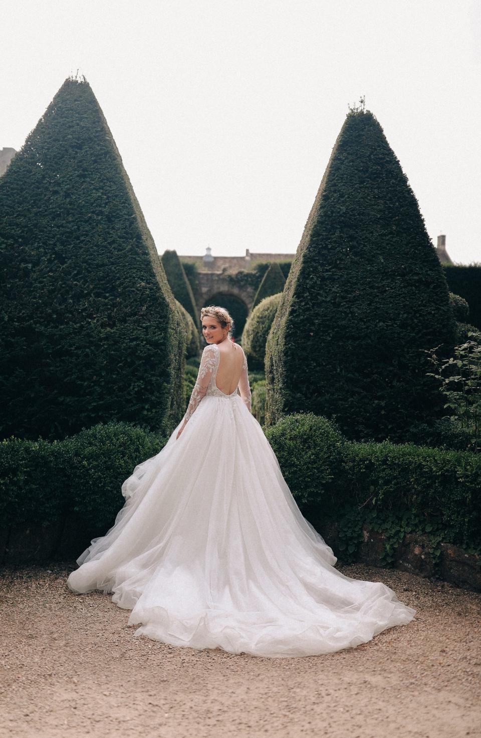 A person looks over their shoulder in a garden wearing a wedding dress.