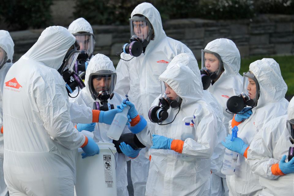 Workers from a Servpro disaster recovery team wearing protective suits and respirators are given supplies as they line up before entering the Life Care Center in Kirkland, Wash., to begin cleaning and disinfecting the facility, Wednesday, March 11, 2020. The nursing home is at the center of the coronavirus outbreak in Washington state.