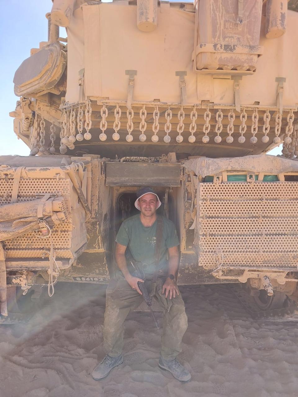 Yoav Atzmoni holding a rifle and sitting on his tank
