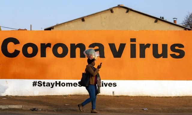 A woman wearing a face mask passes a coronavirus sign (Themba Hadebe/AP)