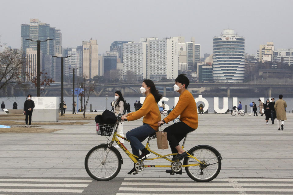 A couple wearing face masks rides a bicycle at a park in Seoul, South Korea, Saturday, March 7, 2020. The number of infections of the COVID-19 disease spread around the globe. (AP Photo/Ahn Young-joon)