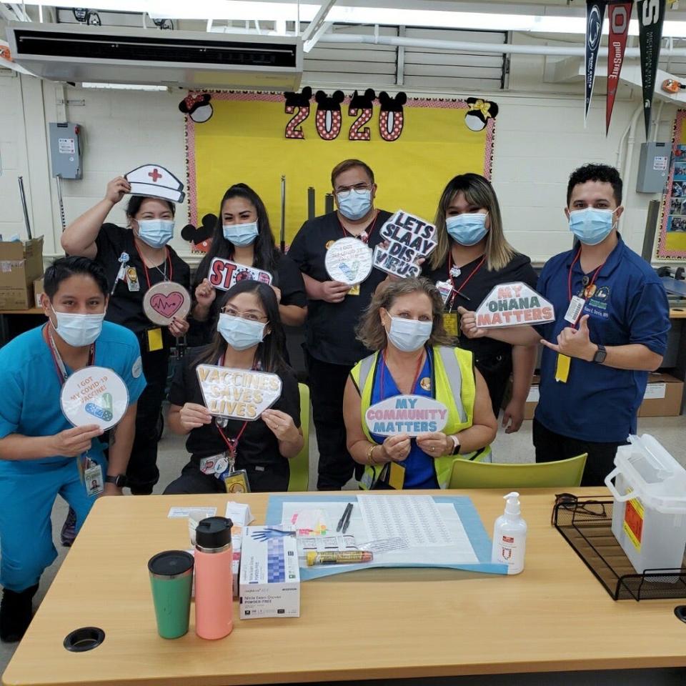 Holding up laminated signs with various phrases such as "My Ohana Matters" to help encourage vaccinations, staff at a school in Honolulu County's Waianae pose for a photo during a vaccine event.