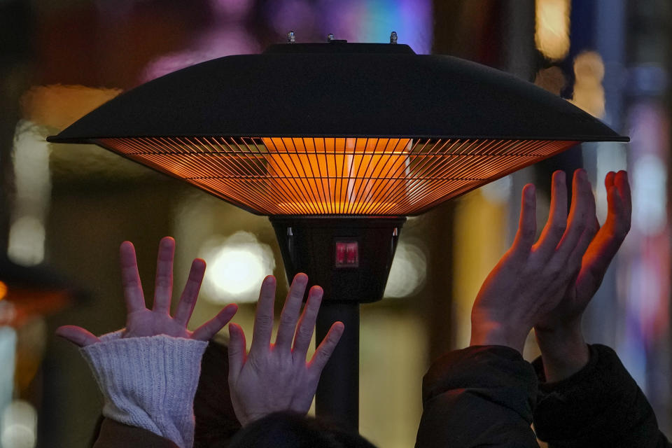 People try to keep warm their hands by a heater as they wait for their seats outside a restaurant at an outdoor shopping mall in Beijing, Saturday, Dec. 23, 2023. A cold wave began earlier in the week bringing extensive snowfall and freezing temperatures across China. (AP Photo/Andy Wong)