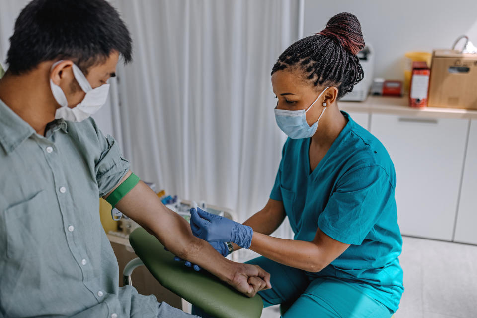 A nurse with a surgical mask on taking a patient's blood