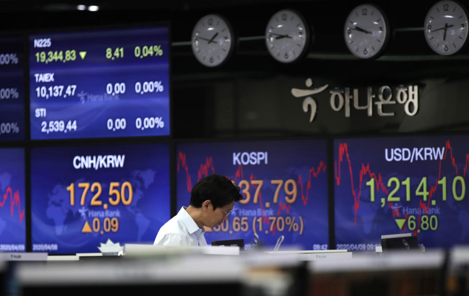 A currency trader walks by the screens showing the Korea Composite Stock Price Index (KOSPI) and the foreign exchange rates at the foreign exchange dealing room in Seoul, South Korea, Thursday, April 9, 2020. Asian shares are mixed, with Tokyo lower, as an overnight rally on Wall Street faded.(AP Photo/Lee Jin-man)