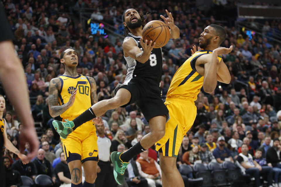 San Antonio Spurs guard Patty Mills (8) lays the ball up as Utah Jazz's Jordan Clarkson (00) and Tony Bradley, right, defend during the first half of an NBA basketball game Friday, Feb. 21, 2020, in Salt Lake City. (AP Photo/Rick Bowmer)