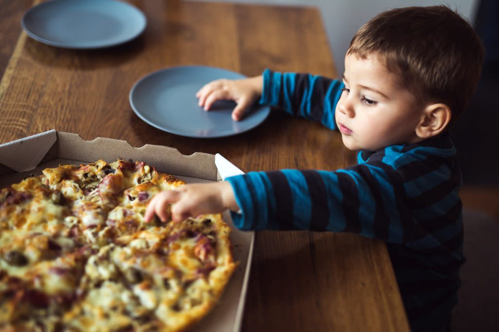 A little boy grabs a slice of pizza while sitting at the dining room table.