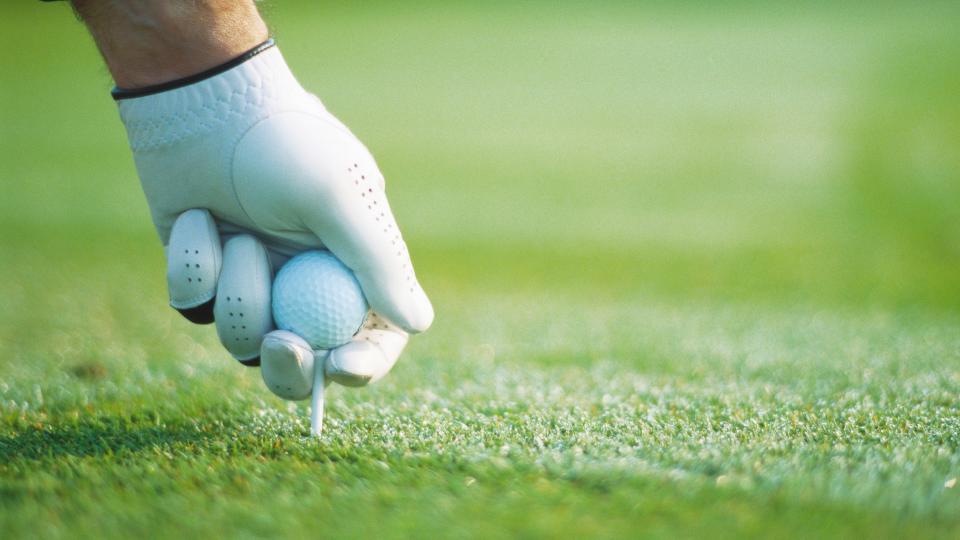   A golfer puts a golf ball on a tee 