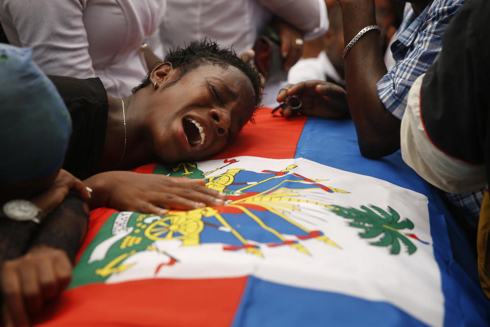 A woman cries on a flag-draped coffin that contain the remains of a 16-year-old boy killed during a month of demonstrations aimed at ousting President Jovenel Moïse, at a joint funeral in a public plaza near the National Palace in Port-au-Prince, Haiti, Wednesday, Oct. 16, 2019. Funerals for 11 of at least 20 people killed were held in six cities, including the capital of Port-au-Prince, where at least two people were injured in a protest that broke out when presidential guards tried to block a road near where hundreds had gathered around the coffins of two victims. (AP Photo/Rebecca Blackwell)