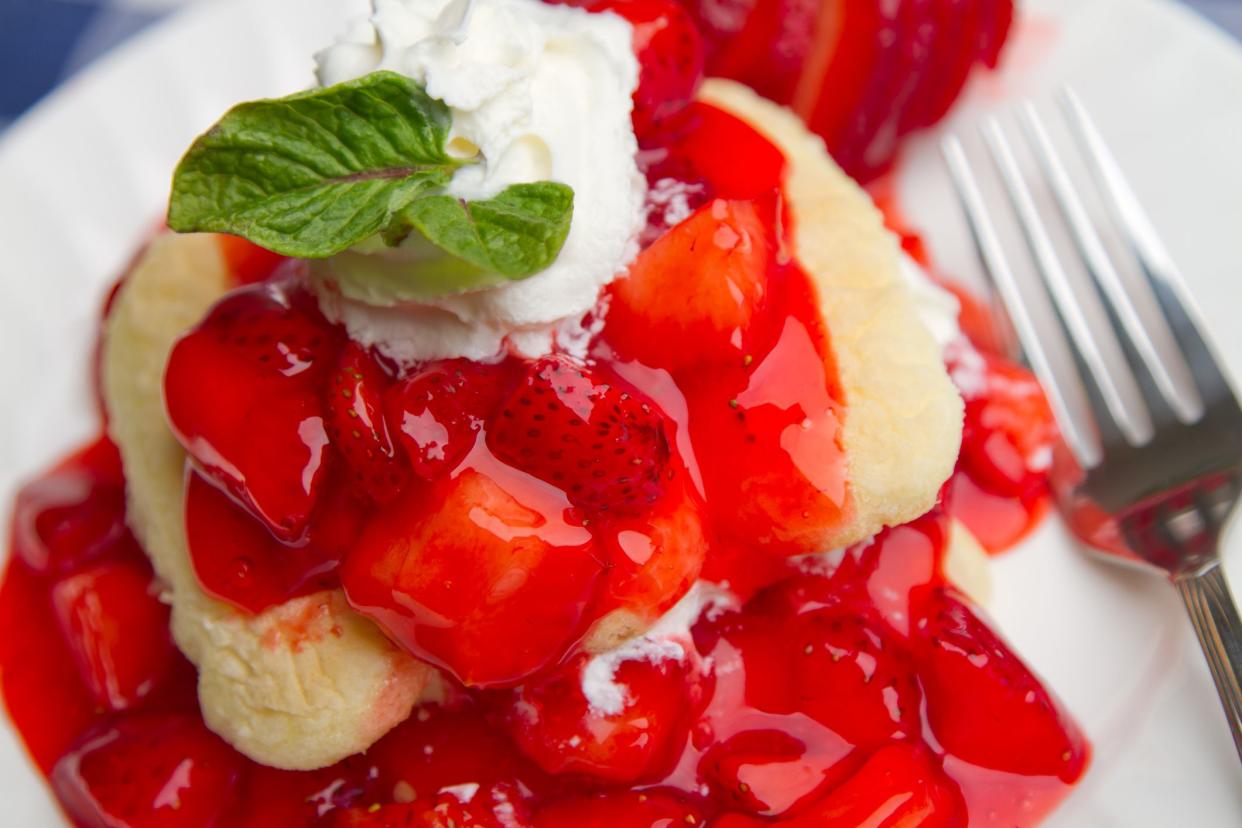 Closeup of angel food cake with strawberry sauce topping and whipped cream on a white plate with a fork