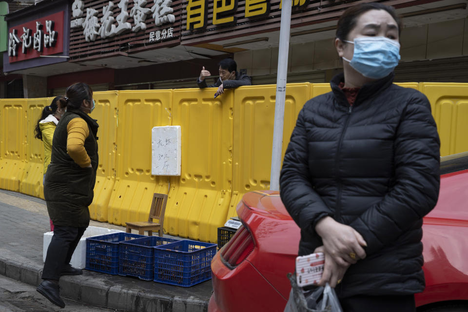 A vendor chats with residents across barriers used to seal off a neighborhood in Wuhan in central China's Hubei province on Friday, April 3, 2020. Sidewalk vendors wearing face masks and gloves sold pork, tomatoes, carrots and other vegetables to shoppers Friday in the Chinese city where the coronavirus pandemic began as workers prepared for a national memorial this weekend for health workers and others who died in the outbreak. (AP Photo/Ng Han Guan)