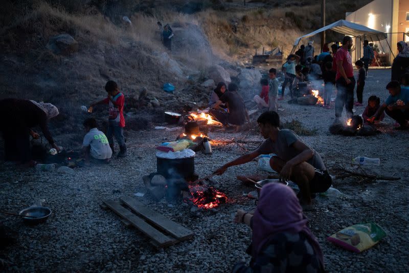 Refugees and migrants from the destroyed Moria camp cook over a fire, on the island of Lesbos