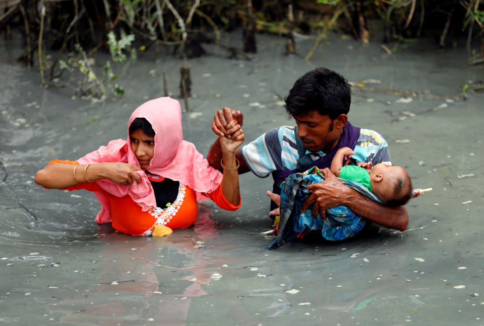 <p>Rohingya refugees carry their child as they walk through water after crossing border by boat through the Naf River in Teknaf, Bangladesh, Sept. 7, 2017. (Photo: Mohammad Ponir Hossain/Reuters) </p>