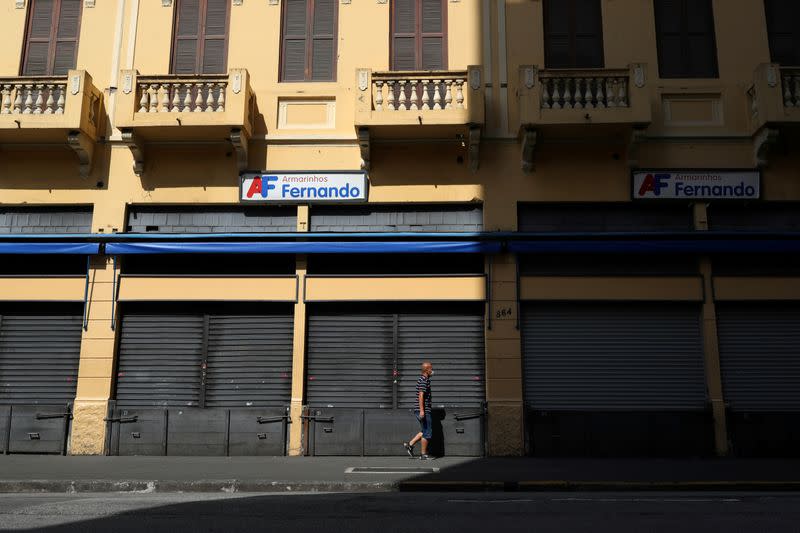 FILE PHOTO: A man wearing protective face mask walks in front of closed stores after the city government decreed the closure of shops and stores as a precautionary measure against coronavirus disease (COVID-19) in downtown Sao Paulo