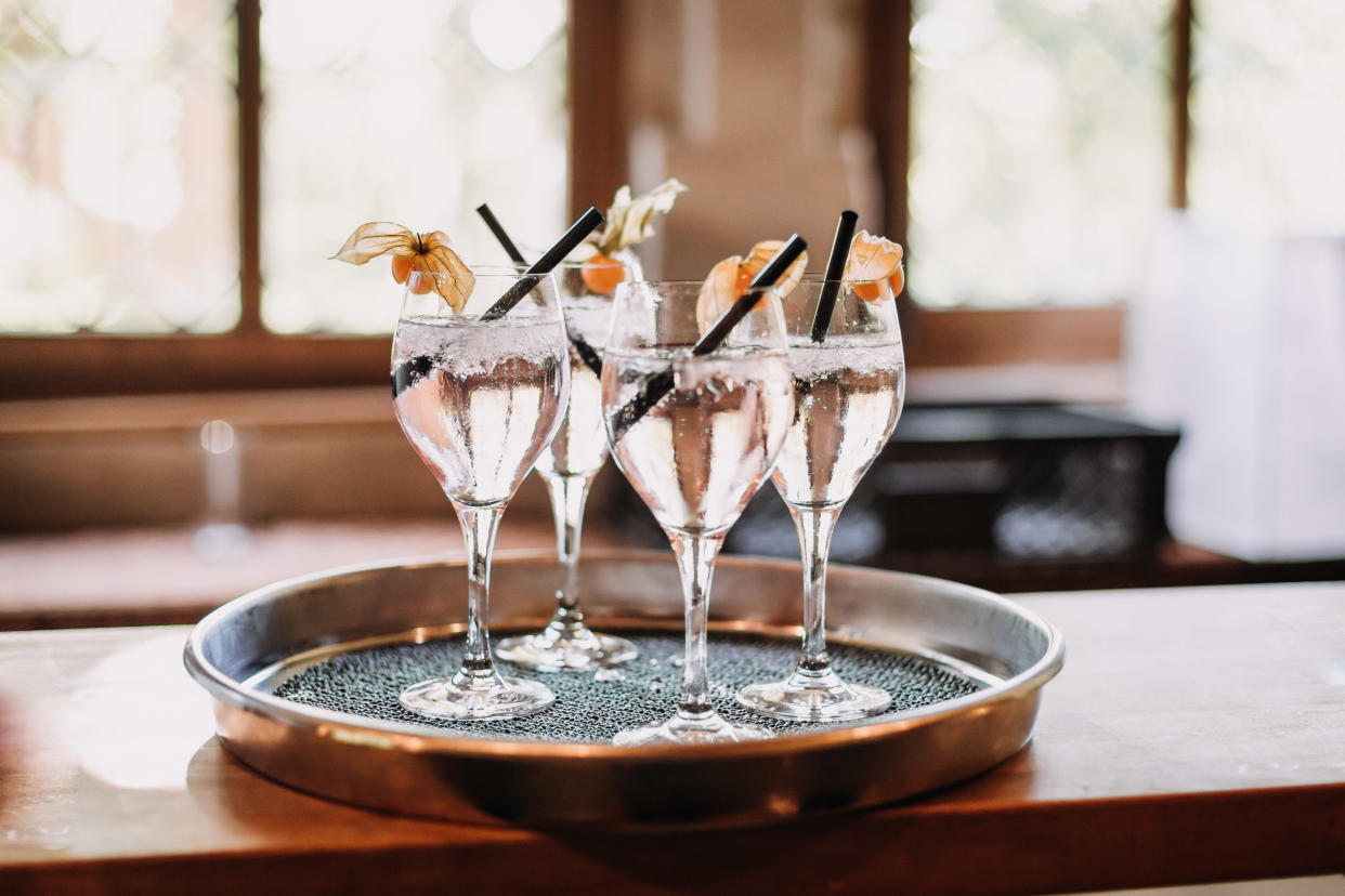 four clinking champagne glasses with transparent sparkling spritzer, Weinschorle on tray salver at a summer wedding party