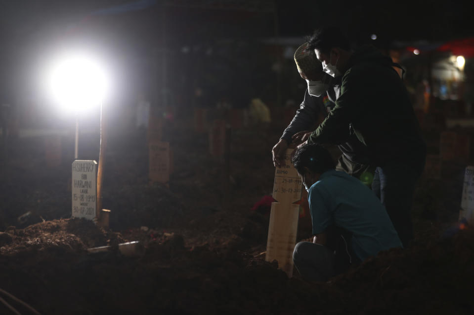 Family members react during the burial of their relative at the special section of the Pedurenan cemetery designated to accommodate the surge in deaths during the coronavirus outbreak in Bekasi, West Java, Indonesia, Friday, July 30, 2021. Indonesia surpassed the grim milestone of 100,000 official COVID-19 deaths on Wednesday, Aug. 4, 2021, as the country struggles with its worst pandemic year fueled by the delta variant, with growing concerns that the actual figure could be much higher with people also dying at home. (AP Photo/Achmad Ibrahim)