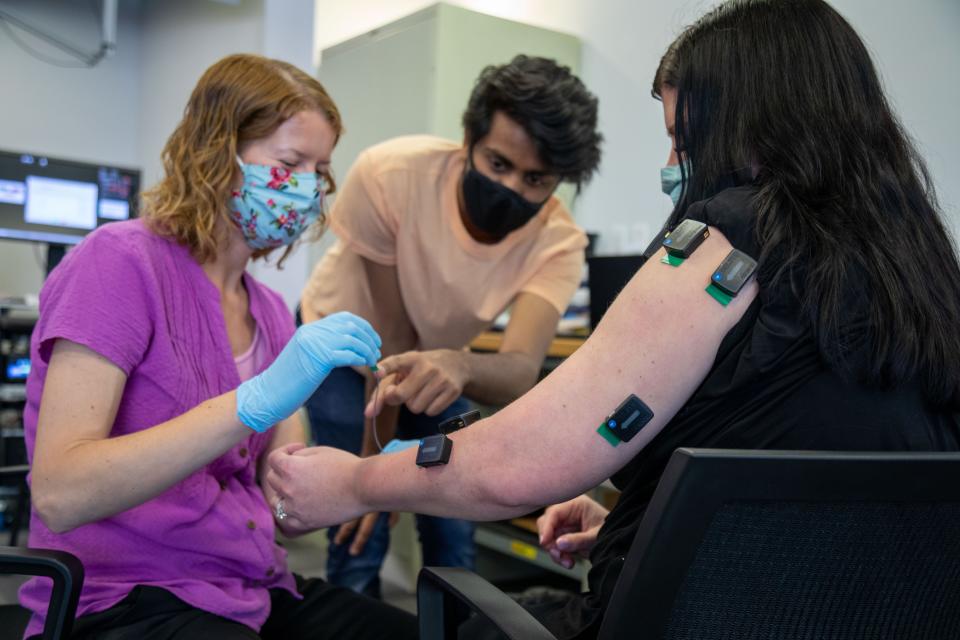 Amy Boos, left, is a kinematic occupational therapist at University of Pittsburgh. Carnegie Mellon University graduate student Nikhil Verma, middle, works with Boos to connect muscle activation sensors on the arm of Heather Rendulic at Rehab Neural Engineering Labs at the University of Pittsburgh.